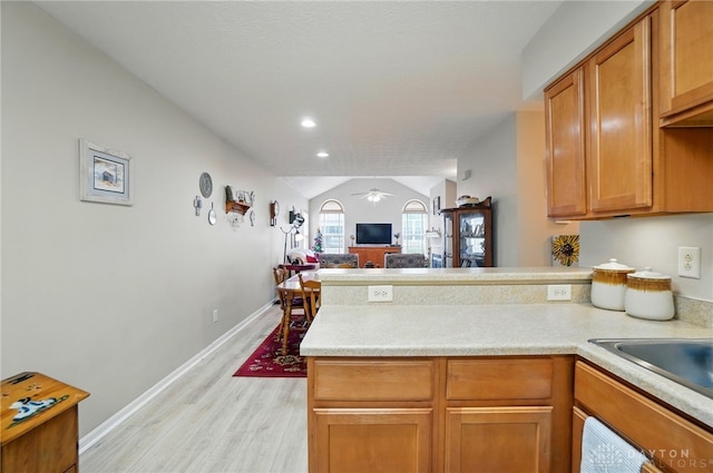 kitchen featuring a peninsula, light wood-type flooring, a ceiling fan, light countertops, and lofted ceiling
