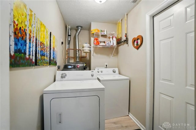 clothes washing area featuring independent washer and dryer, light wood-type flooring, a textured ceiling, and water heater