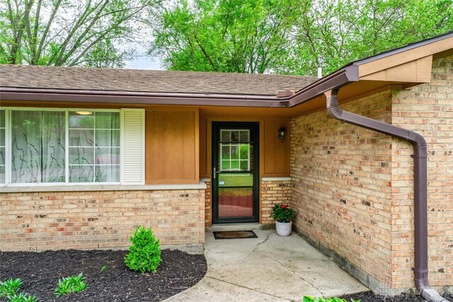 doorway to property featuring brick siding and a shingled roof