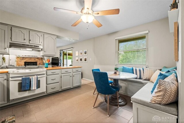 kitchen with white gas range oven, under cabinet range hood, light countertops, ceiling fan, and gray cabinets
