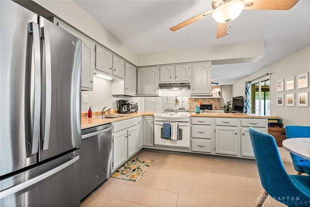 kitchen with appliances with stainless steel finishes, a sink, a peninsula, under cabinet range hood, and light countertops