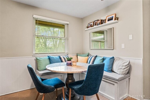 dining space featuring breakfast area, healthy amount of natural light, a wainscoted wall, and tile patterned floors