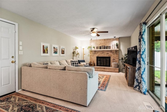 living area featuring a brick fireplace, a ceiling fan, healthy amount of natural light, light colored carpet, and a textured ceiling