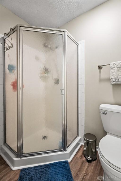 bathroom featuring wood finished floors, a shower stall, toilet, and a textured ceiling