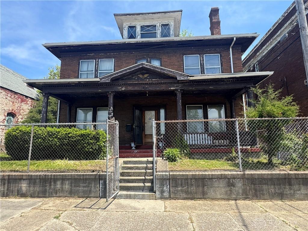 416 N Conover St, Dayton, OH 45402 - traditional style home featuring brick siding, a porch, a fenced front yard, and a chimney