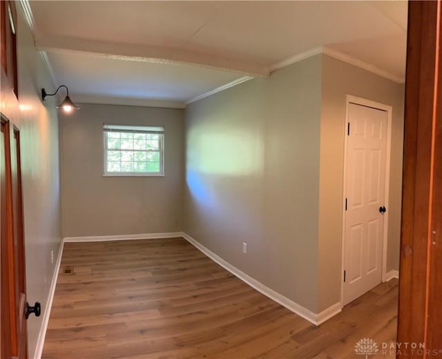 empty room featuring crown molding, wood finished floors, and baseboards