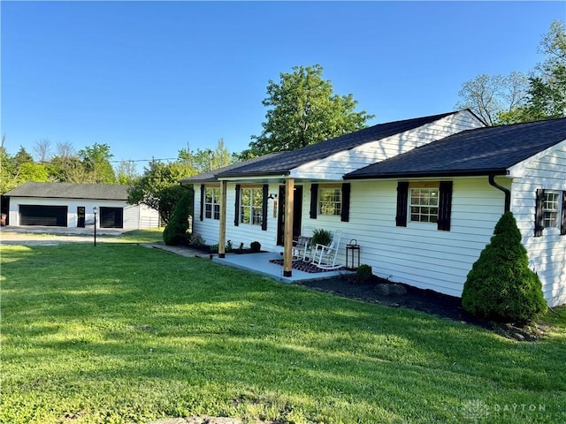 view of front of home with a front lawn, covered porch, a garage, a shingled roof, and an outbuilding