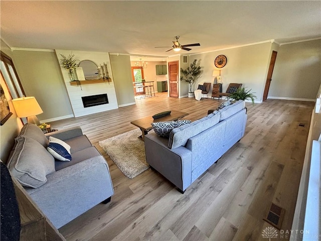living room featuring crown molding, wood finished floors, ceiling fan, baseboards, and a fireplace
