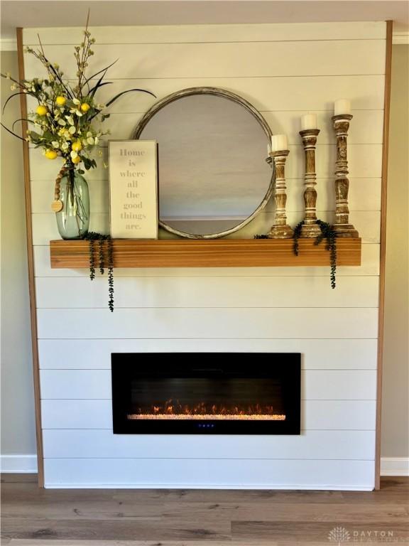 detailed view of a lit fireplace, baseboards, and wood finished floors