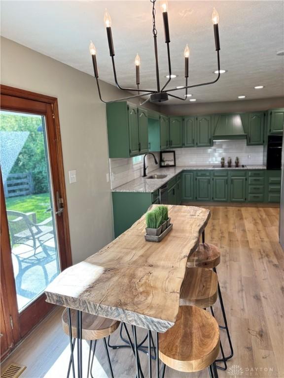 kitchen with green cabinets, a sink, a chandelier, custom exhaust hood, and black appliances