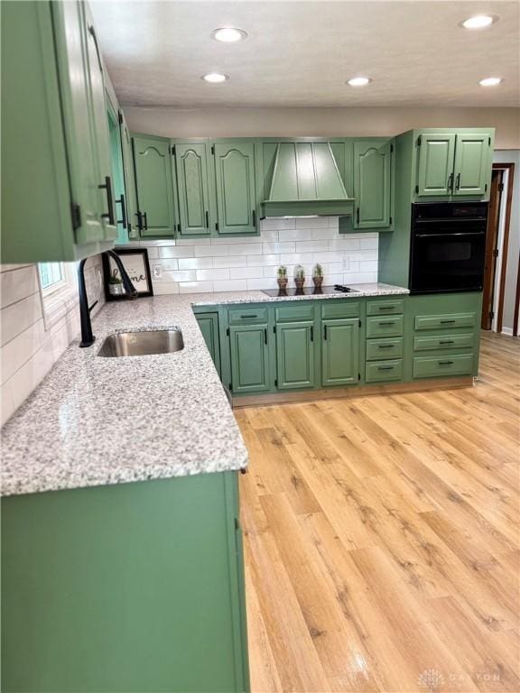 kitchen with black appliances, custom exhaust hood, a sink, green cabinetry, and backsplash