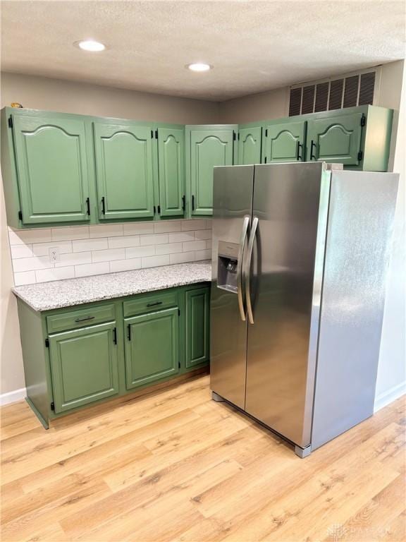 kitchen featuring stainless steel fridge with ice dispenser, light countertops, light wood-type flooring, tasteful backsplash, and a textured ceiling