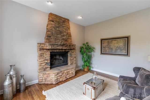 living room with baseboards, a stone fireplace, and wood finished floors