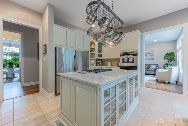 kitchen featuring stainless steel appliances, light tile patterned floors, glass insert cabinets, decorative backsplash, and a chandelier