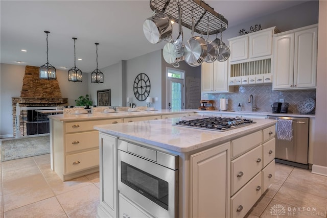 kitchen featuring appliances with stainless steel finishes, a peninsula, a kitchen island, tasteful backsplash, and light tile patterned floors