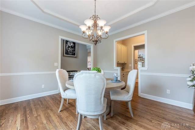 dining area featuring a chandelier, wood finished floors, ornamental molding, baseboards, and a raised ceiling