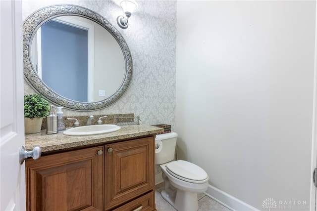 half bathroom featuring wallpapered walls, toilet, vanity, tile patterned floors, and baseboards