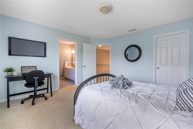 bedroom with light colored carpet, baseboards, an office area, and ensuite bathroom