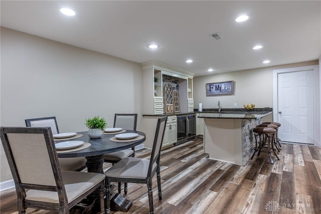 kitchen with a peninsula, dark wood-type flooring, a kitchen breakfast bar, recessed lighting, and a sink
