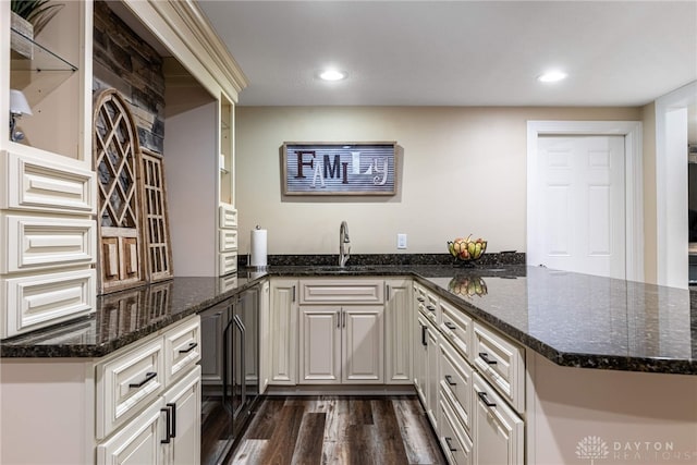 kitchen featuring a peninsula, dark wood-style flooring, dark stone countertops, recessed lighting, and a sink