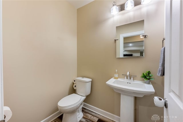 half bath with toilet, baseboards, and wood finished floors