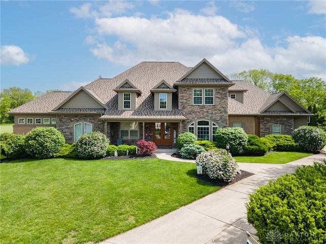 view of front of home with stone siding, a front yard, covered porch, and a shingled roof