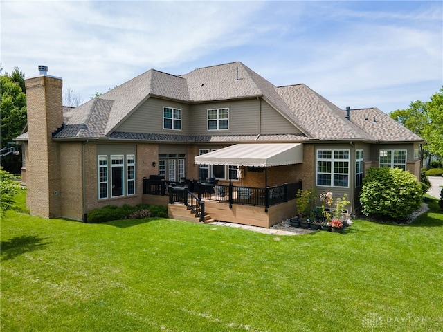 back of property featuring a wooden deck, a chimney, a lawn, and a shingled roof