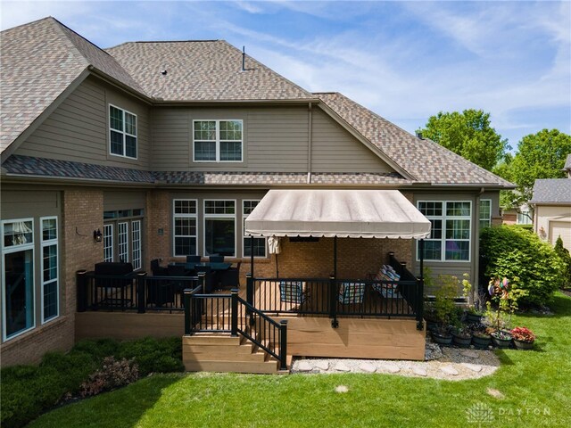 back of property with brick siding, a lawn, a deck, and a shingled roof