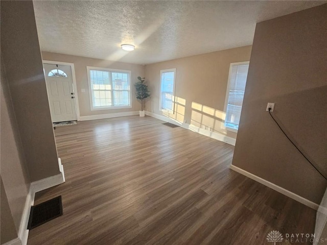 unfurnished living room with baseboards, dark wood-type flooring, and a textured ceiling