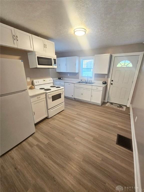 kitchen featuring white appliances, a textured ceiling, a sink, white cabinets, and light wood-style flooring