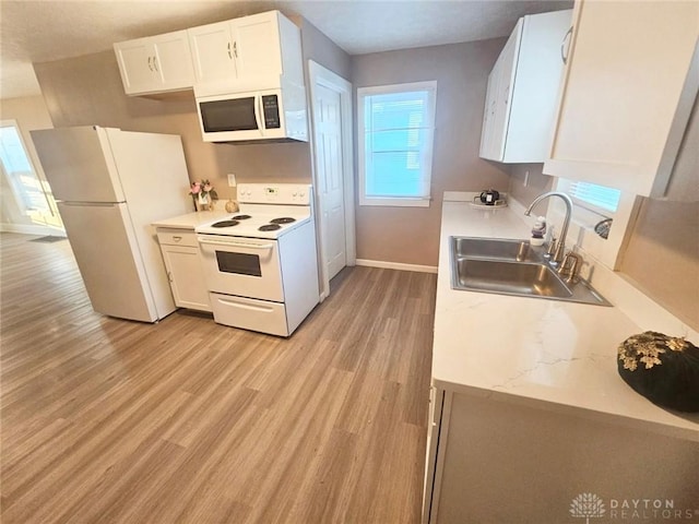 kitchen featuring white appliances, a sink, light wood-type flooring, baseboards, and white cabinetry