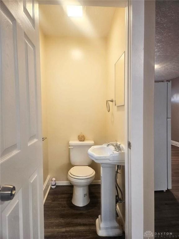 bathroom with wood finished floors, toilet, baseboards, a sink, and a textured ceiling