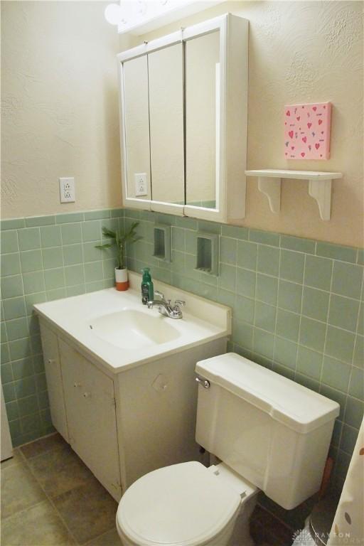 half bath with tile walls, toilet, vanity, and a wainscoted wall