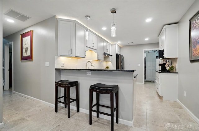 kitchen with black microwave, a peninsula, freestanding refrigerator, backsplash, and under cabinet range hood