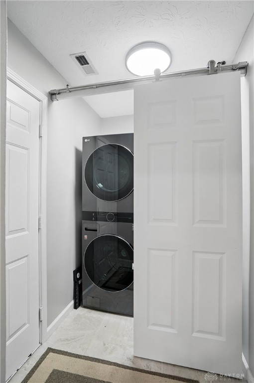 washroom with estacked washer and dryer, baseboards, and a textured ceiling