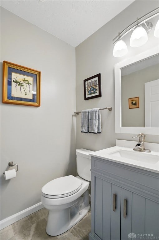 half bath featuring toilet, vanity, baseboards, and a textured ceiling