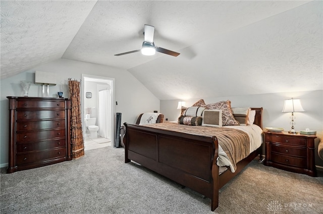 carpeted bedroom with lofted ceiling, a textured ceiling, ensuite bathroom, and a ceiling fan