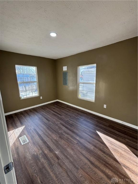 empty room featuring dark wood-style flooring, baseboards, healthy amount of natural light, a textured ceiling, and recessed lighting