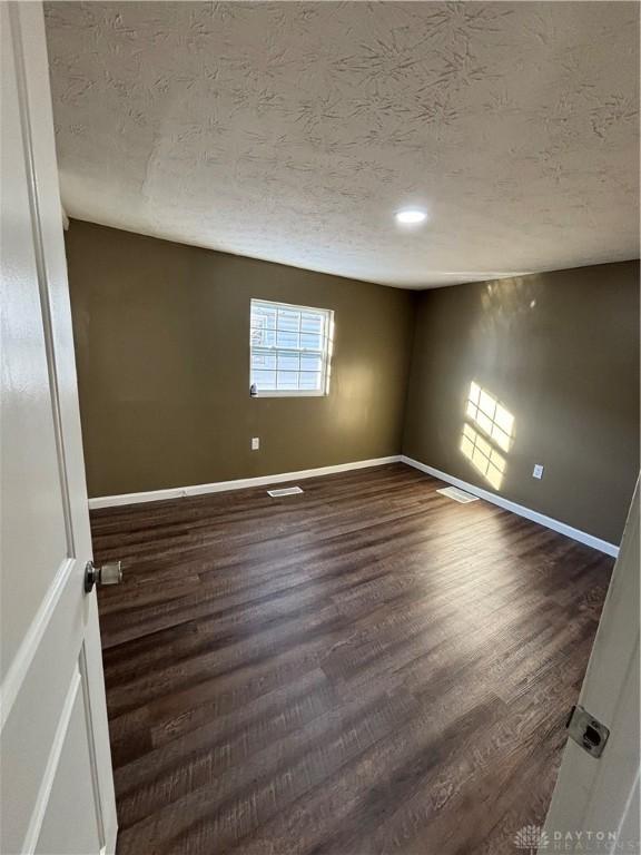 spare room with a textured ceiling, baseboards, dark wood-type flooring, and recessed lighting