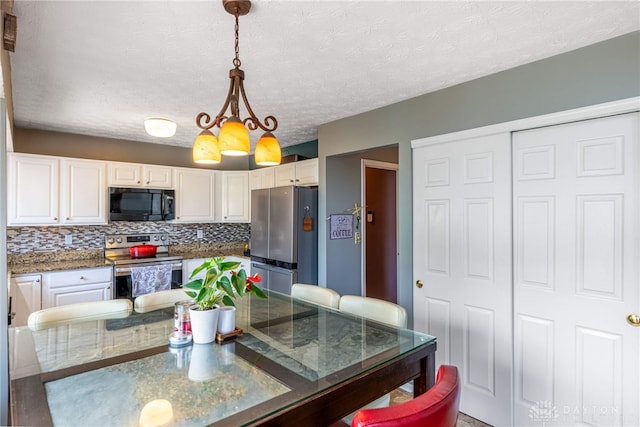 kitchen with stainless steel appliances, white cabinetry, pendant lighting, decorative backsplash, and dark stone counters