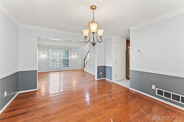 empty room featuring a chandelier, light wood-style floors, baseboards, and ornamental molding