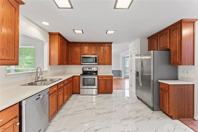 kitchen with appliances with stainless steel finishes, a sink, recessed lighting, light countertops, and brown cabinetry