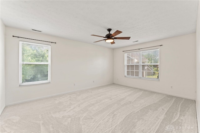 unfurnished room featuring healthy amount of natural light, a ceiling fan, light colored carpet, baseboards, and a textured ceiling