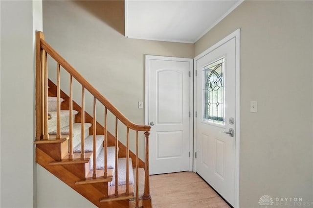entryway with light wood-type flooring, ornamental molding, and stairs