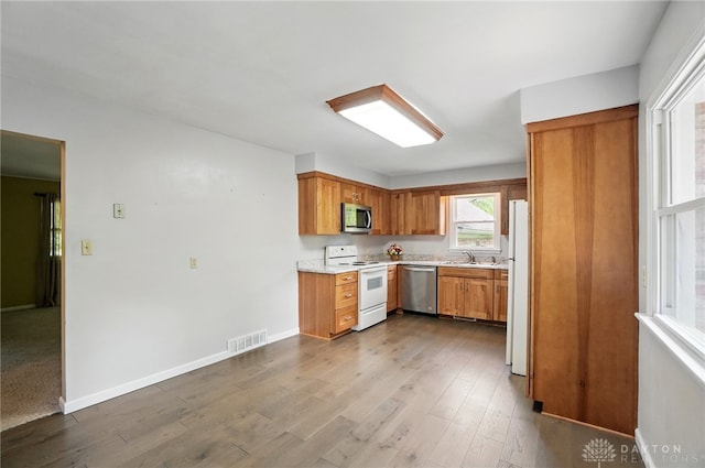 kitchen featuring stainless steel appliances, a sink, light countertops, brown cabinetry, and dark wood finished floors