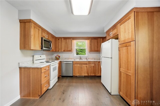 kitchen featuring appliances with stainless steel finishes, a sink, wood finished floors, and brown cabinets