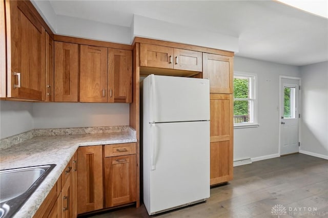 kitchen featuring freestanding refrigerator, a sink, wood finished floors, and brown cabinets