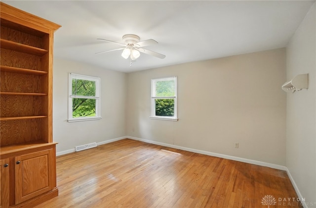 empty room with plenty of natural light, a ceiling fan, baseboards, and light wood finished floors