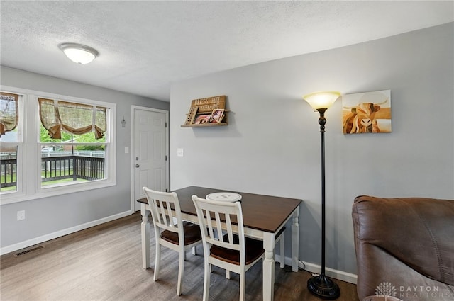 dining space with wood finished floors, a textured ceiling, and baseboards