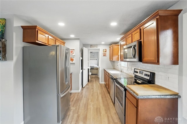 kitchen featuring stainless steel appliances, a sink, light wood finished floors, backsplash, and recessed lighting